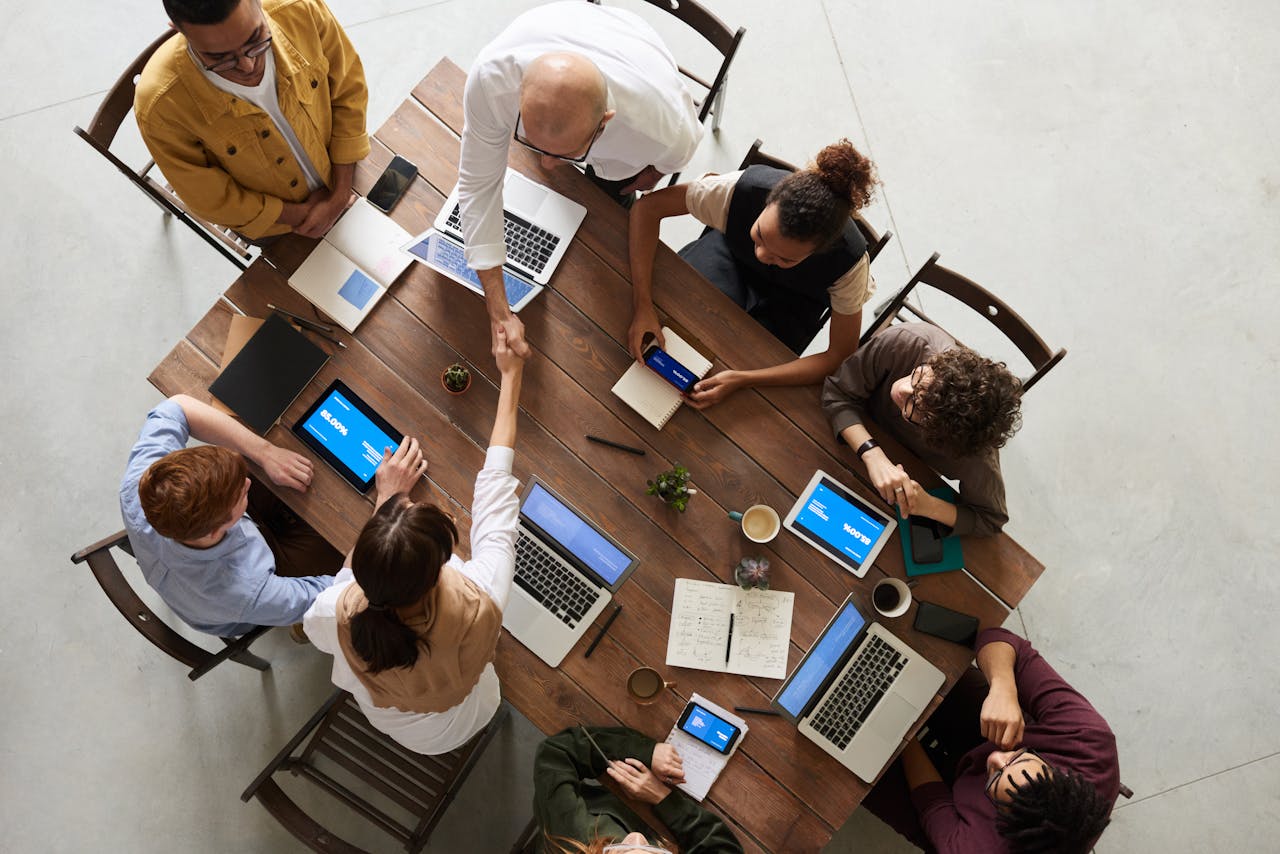gallery-4 Top view of a diverse team collaborating in an office setting with laptops and tablets, promoting cooperation.