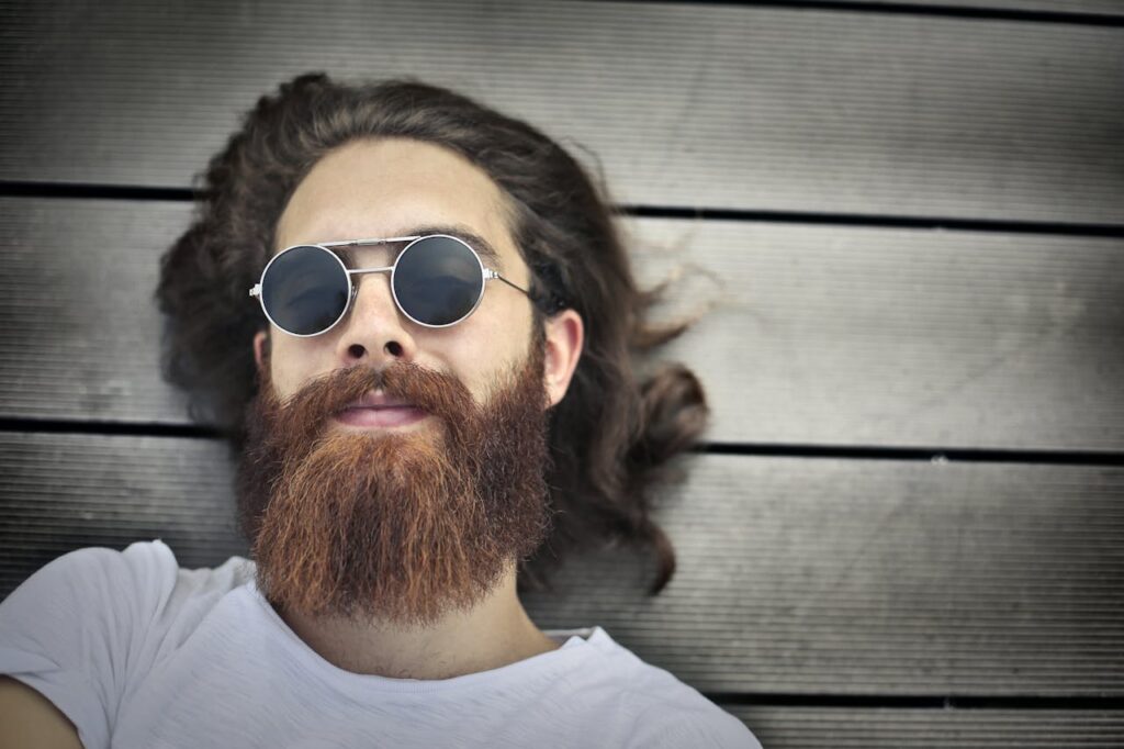 pexels photo 3779668 Portrait of a relaxed bearded man wearing sunglasses while lying down on a wooden floor. Ideal for lifestyle themes.